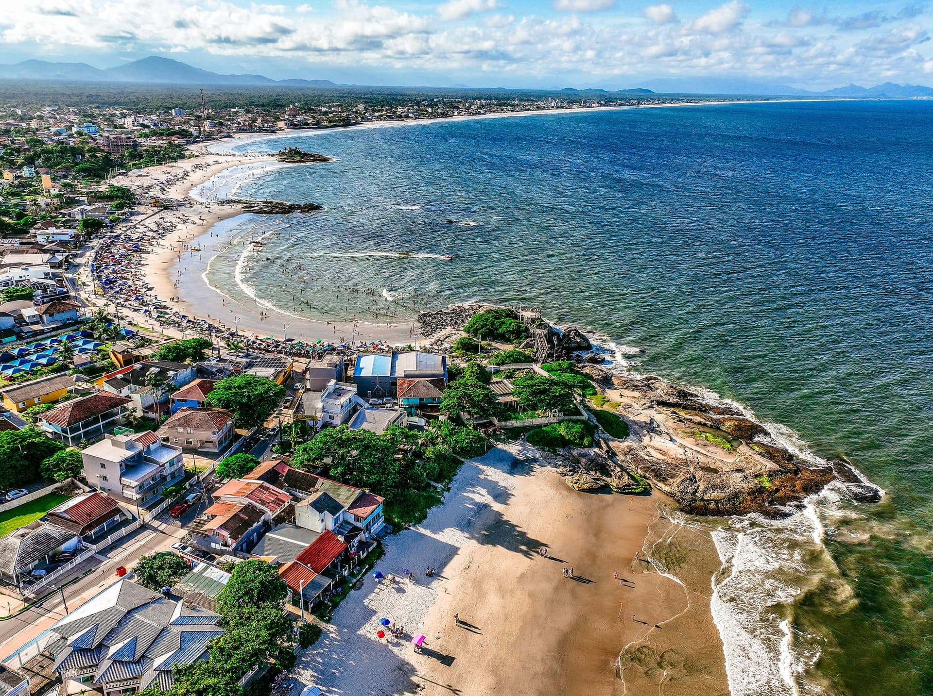 Vista aérea do litoral de Itapoá, em Santa Catarina, com a praia, a mata e a ocupação urbana.